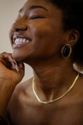 Woman wearing a gold necklace and black earrings with a neutral background